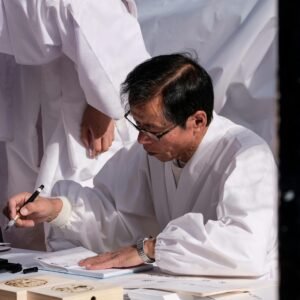 A man in traditional attire practices Japanese calligraphy during a cultural ceremony.