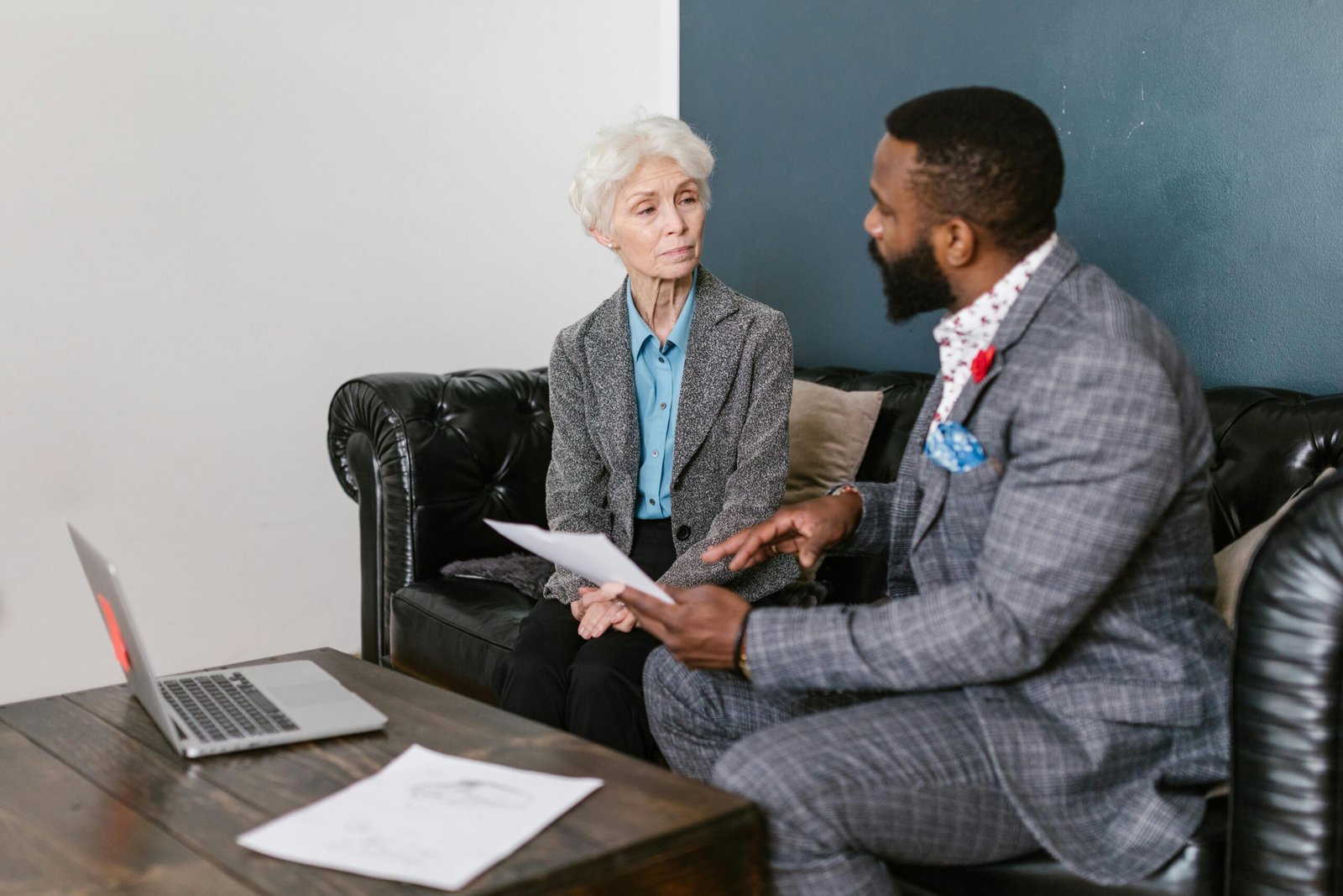 An elderly woman and a man in a professional meeting discussing documents indoors.