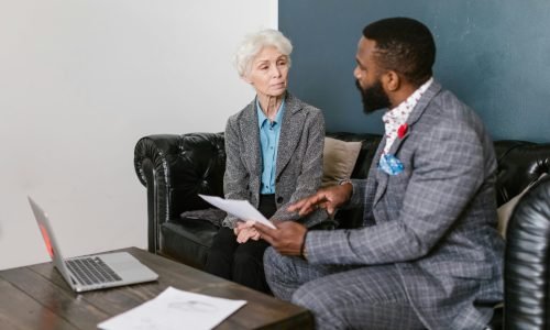 An elderly woman and a man in a professional meeting discussing documents indoors.